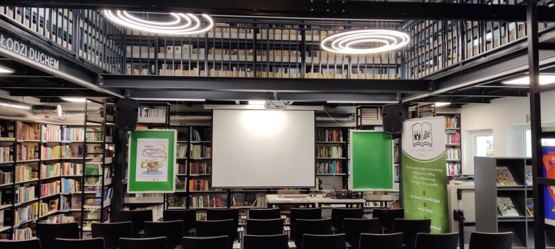 sala biblioteczna z regałami książek, krzesłami i ekranem