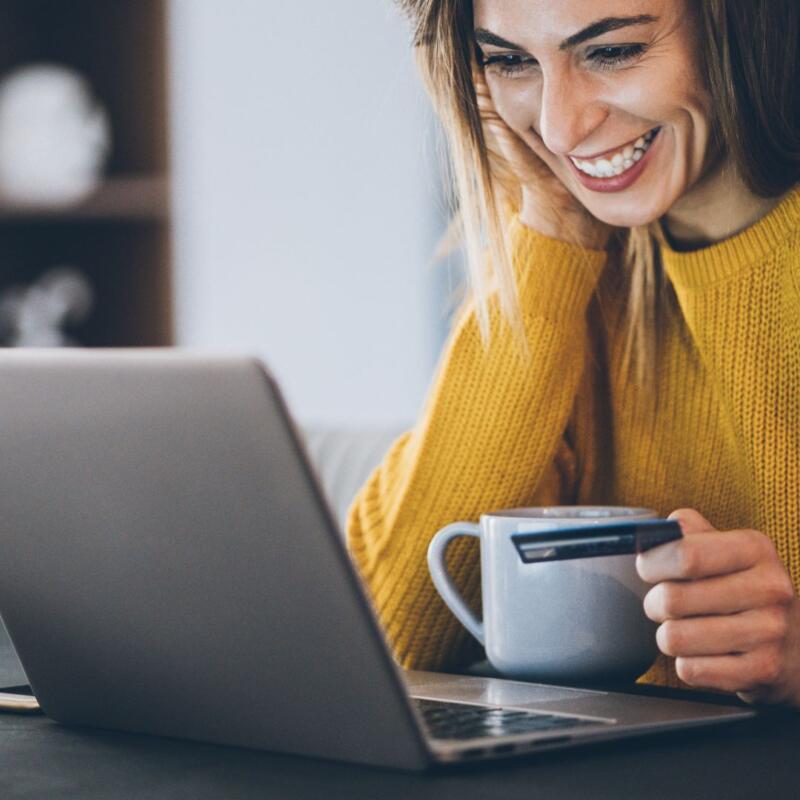 uśmiechnięta kobieta przed laptopem trzymająca kartę kredytową